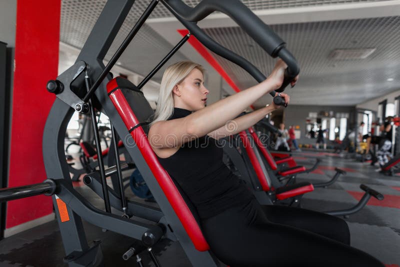 Атлетическая молодая женщина в черном современном sportswear приниманнсяое за усаживание на имитаторе в студии фитнеса стоковое изображение Атлетическая молодая женщина в черном современном sportswear приниманнсяое за усаживание на имитаторе в студии фитнеса стоковое изображение