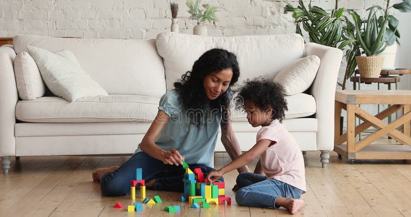 Афро американская мать играет строителя с дошкольной дочерью на полу