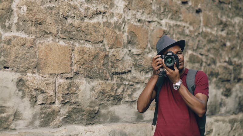 Афро-американское счастливое туристское принимая фото на его камере dslr Молодой человек стоя около известного здания в Европе стоковые изображения Афро-американское счастливое туристское принимая фото на его камере dslr Молодой человек стоя около известного здания в Европе стоковые изображения
