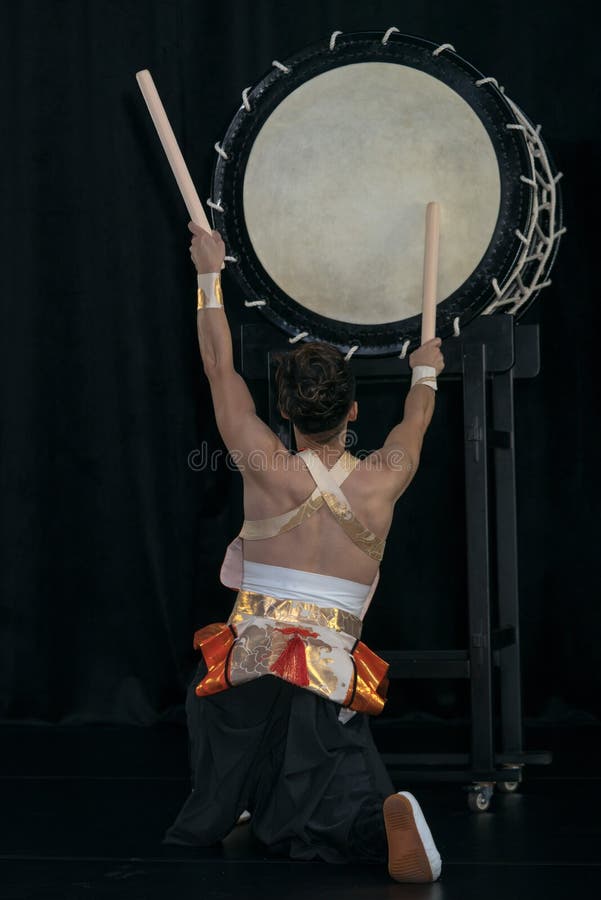 Taiko drummer hits the big drum on stage on a black background, back view. Taiko drummer hits the big drum on stage on a black background, back view