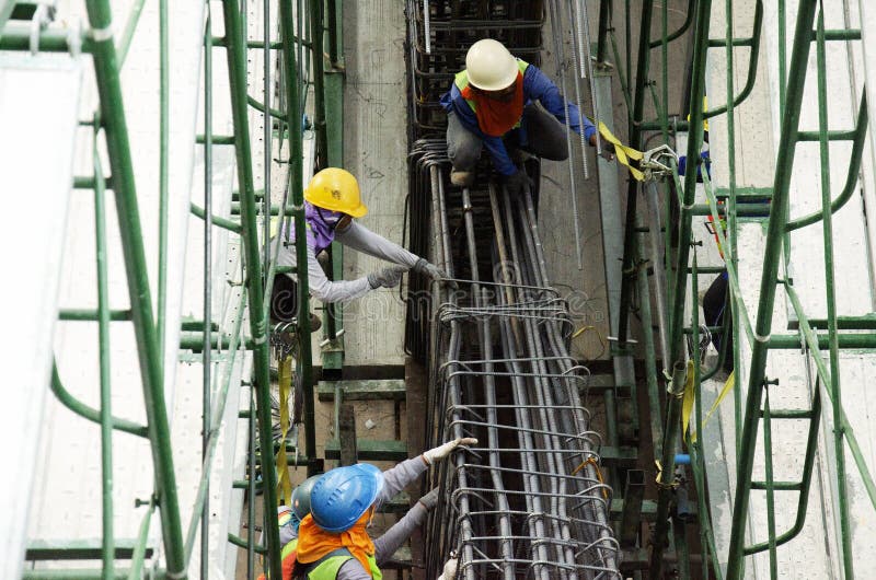 Бары металлических стержней азиатского работника людей вязать в подкрепление рамок для конкретный лить на строительной площадке