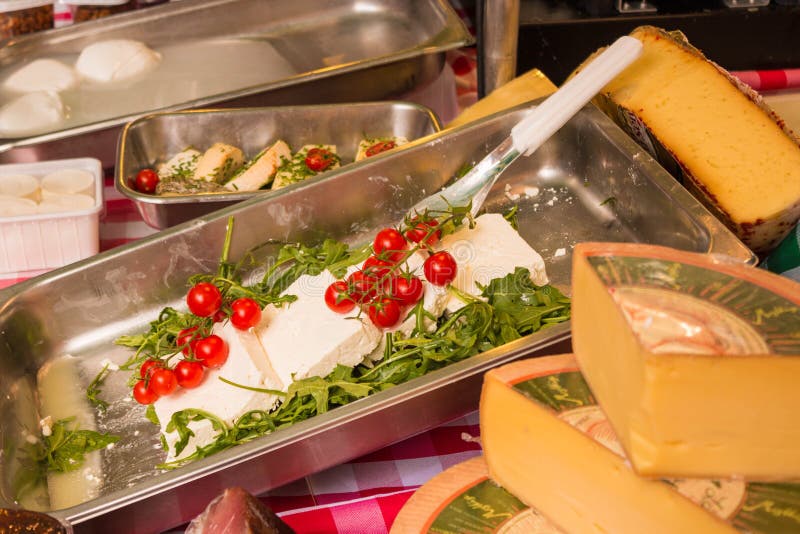 Salzburg, Austria - June 1, 2017: White cheese with cherry tomatoes and rucola surrounded by other various kinds of cheese for sale on farmers market. Salzburg, Austria - June 1, 2017: White cheese with cherry tomatoes and rucola surrounded by other various kinds of cheese for sale on farmers market.