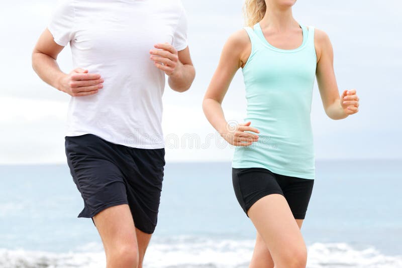 Runners - people running on beach. Midsection close up of unrecognizable young couple jogging training at boardwalk by ocean sea. Runners - people running on beach. Midsection close up of unrecognizable young couple jogging training at boardwalk by ocean sea.