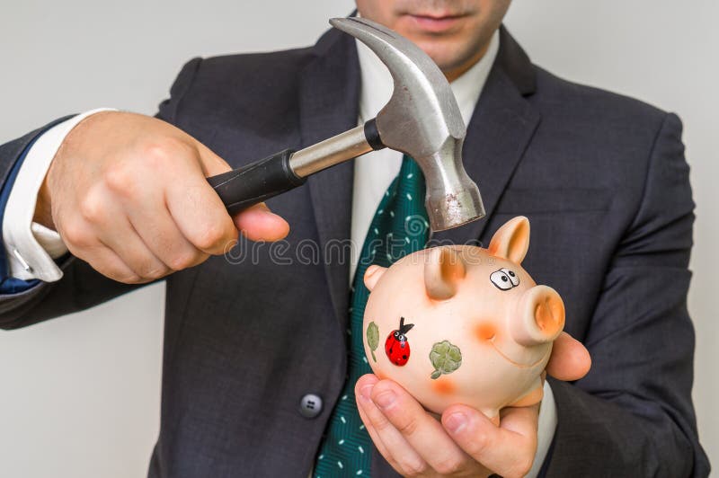 Hopeless businessman breaking piggy bank with iron hammer. Hopeless businessman breaking piggy bank with iron hammer