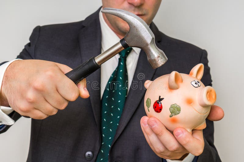 Hopeless businessman breaking piggy bank with iron hammer. Hopeless businessman breaking piggy bank with iron hammer