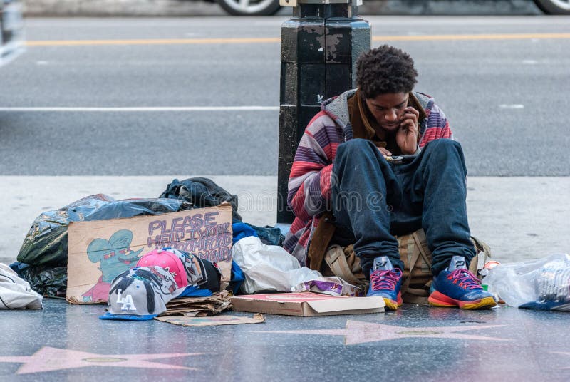 Los Angeles, California, United States of America - January 8, 2017. Homeless man on Sunset Boulevard in Los Angeles, sitting on the ground with his belongings and looking into smartphone. Los Angeles, California, United States of America - January 8, 2017. Homeless man on Sunset Boulevard in Los Angeles, sitting on the ground with his belongings and looking into smartphone