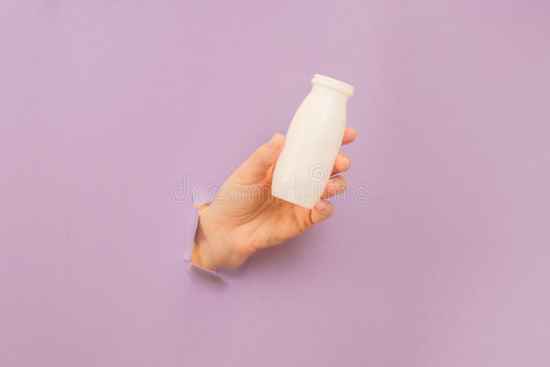 White bottle of probiotic yogurt for digestive system in a hand with lilac background. Dietary supplements for stomach. White bottle of probiotic yogurt for digestive system in a hand with lilac background. Dietary supplements for stomach