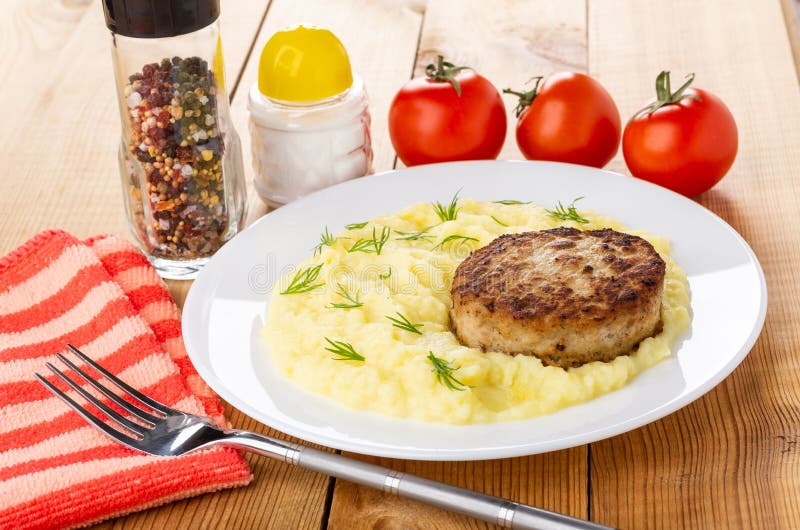 Белая плита с котлетой, картофельным пюре, шейкером соли, condiment, томатами, вилкой на деревянном столе стоковое фото rf Белая плита с котлетой, картофельным пюре, шейкером соли, condiment, томатами, вилкой на деревянном столе стоковое фото rf
