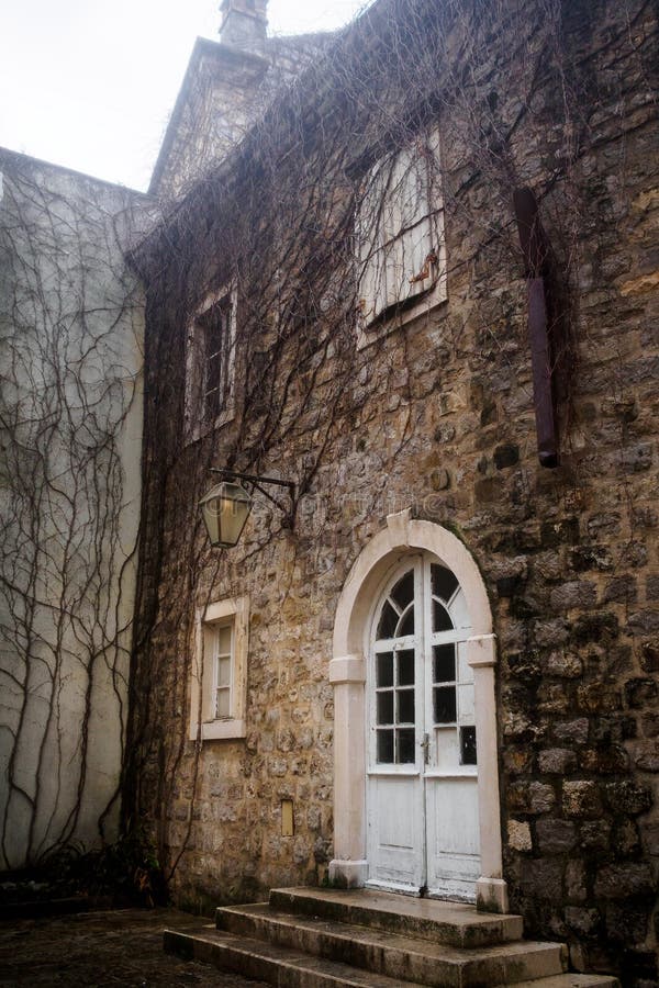 Белая полукруглая дверь со стеклом в каменной стене старого городка в Budva, Черногории стоковая фотография