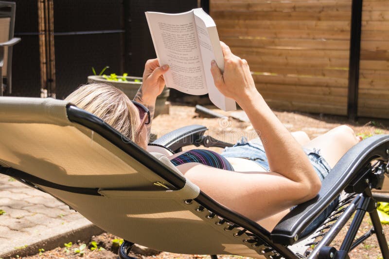 Белокурая книга чтения женщины путем принимать sunbath в задворк дома стоковые изображения Белокурая книга чтения женщины путем принимать sunbath в задворк дома стоковые изображения
