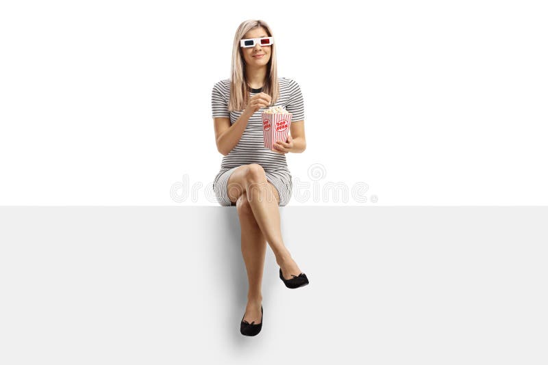 Young blond woman sitting on a panel eating popcorn and wearing 3d glasses isolated on white background. Young blond woman sitting on a panel eating popcorn and wearing 3d glasses isolated on white background