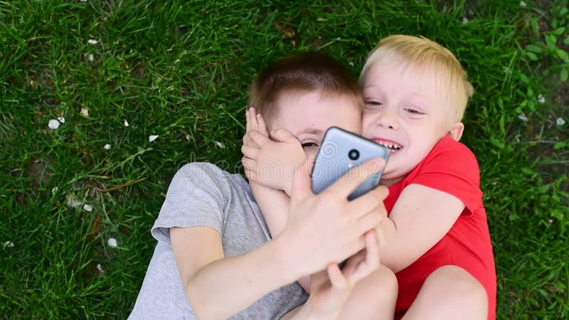 Белокурые и darkhaired мальчики лежали на траве попадая впросак вокруг и принимая selfies. Вид сверху.