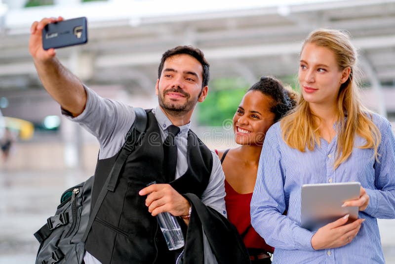 Белый мобильный телефон пользы бизнесмена к selfie со смешанной гонкой и белыми женщинами и все них выглядят счастливыми стоковое фото Белый мобильный телефон пользы бизнесмена к selfie со смешанной гонкой и белыми женщинами и все них выглядят счастливыми стоковое фото