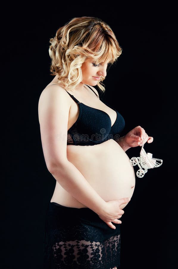 Беременная женщина на черной предпосылке держа pram младенца около tummy