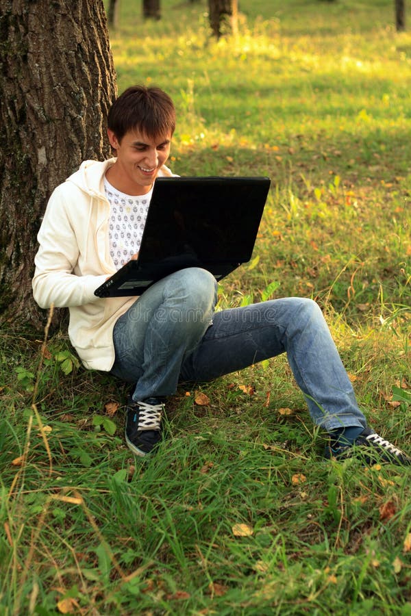 Student sitting by tree works with laptop. Student sitting by tree works with laptop