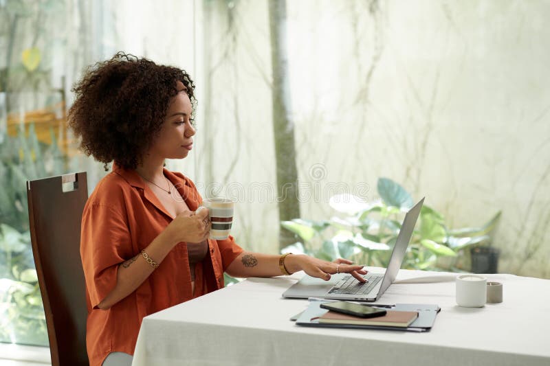 Woman drinking morning coffee and checking e-mails on laptop when working from home. Woman drinking morning coffee and checking e-mails on laptop when working from home