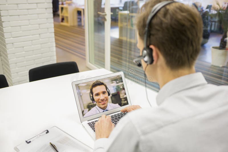 Бизнесмен в офисе на видеоконференции с шлемофоном, Skype стоковое изображение Бизнесмен в офисе на видеоконференции с шлемофоном, Skype стоковое изображение