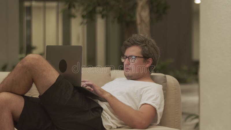 бизнесмен печатает в ноутбуке, лежащем на диване современной гостиной