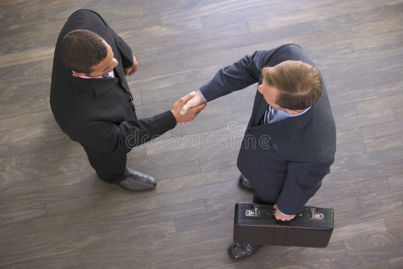 Two businessmen indoors shaking hands wearing suits. Two businessmen indoors shaking hands wearing suits.