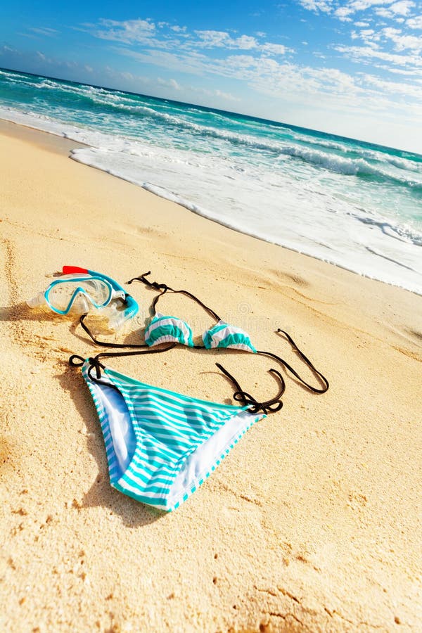 Still life bikini swimsuit and snorkel mask on the beach with footprints on sand and sea on background. Still life bikini swimsuit and snorkel mask on the beach with footprints on sand and sea on background