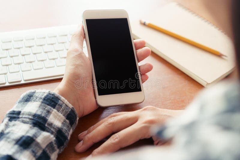 Близкая поднимающая вверх рука используя смартфон на предпосылке стола в офисе В наличии удержание дисплея смартфона пустого стоковая фотография rf