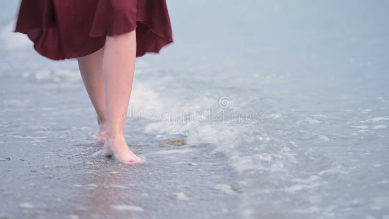 Близкие ноги молодой девушки в красном платье поворачивают волны на мокрый берег моря Переместить из фокуса в фокус
