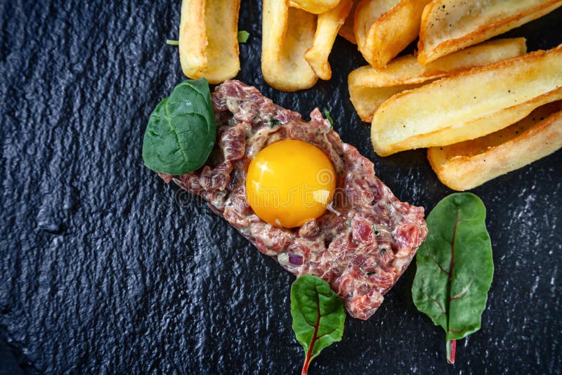 Близкий поднимающий вверх взгляд на телятине tartare служил с зажаренной картошкой, сырцовым яйцом и петрушкой на черной керамиче стоковое фото rf Близкий поднимающий вверх взгляд на телятине tartare служил с зажаренной картошкой, сырцовым яйцом и петрушкой на черной керамиче стоковое фото rf