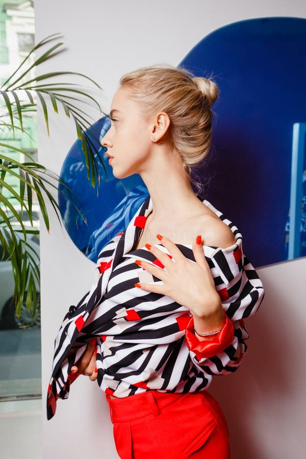 Блоггер маленькой девочки моды одетый в стильной striped рубашке и красных представлениях брюк на предпосылку белого и голубого стоковые фотографии rf Блоггер маленькой девочки моды одетый в стильной striped рубашке и красных представлениях брюк на предпосылку белого и голубого стоковые фотографии rf
