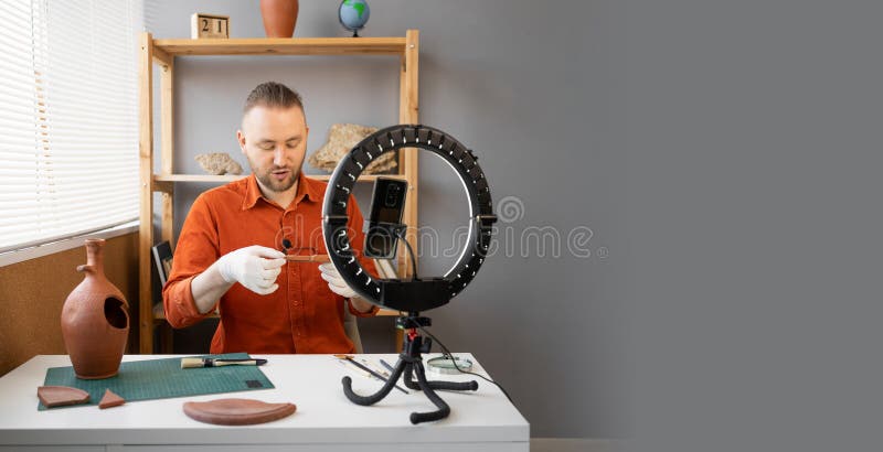 Archaeologist blogger broadcasts live with a ring lamp in his office working with ancient artifacts of prehistoric culture. Banner. Copy space. Archaeologist blogger broadcasts live with a ring lamp in his office working with ancient artifacts of prehistoric culture. Banner. Copy space