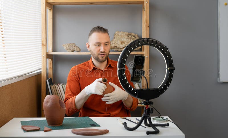 Archaeologist blogger broadcasts live with a ring lamp in his office working with ancient artifacts of prehistoric culture. Copy space. Archaeologist blogger broadcasts live with a ring lamp in his office working with ancient artifacts of prehistoric culture. Copy space