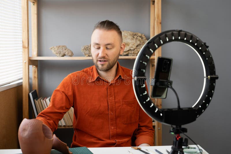 Archaeologist blogger broadcasts live with a ring lamp in his office working with ancient artifacts of prehistoric culture. Copy space. Archaeologist blogger broadcasts live with a ring lamp in his office working with ancient artifacts of prehistoric culture. Copy space