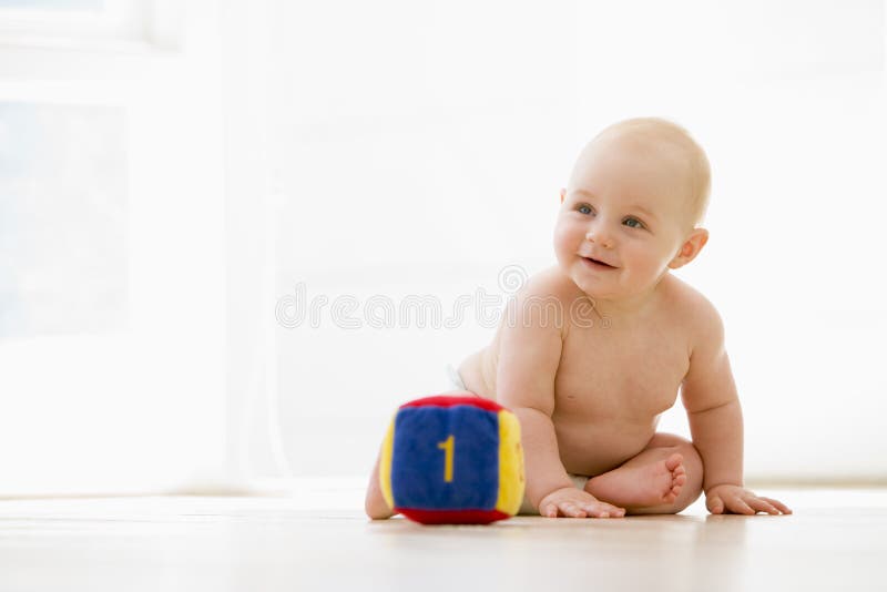 Baby sitting indoors with block smiling away from camera. Baby sitting indoors with block smiling away from camera