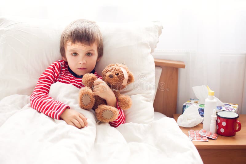 Больной мальчик ребенка лежа в кровати при лихорадка, отдыхая Стоковое .
