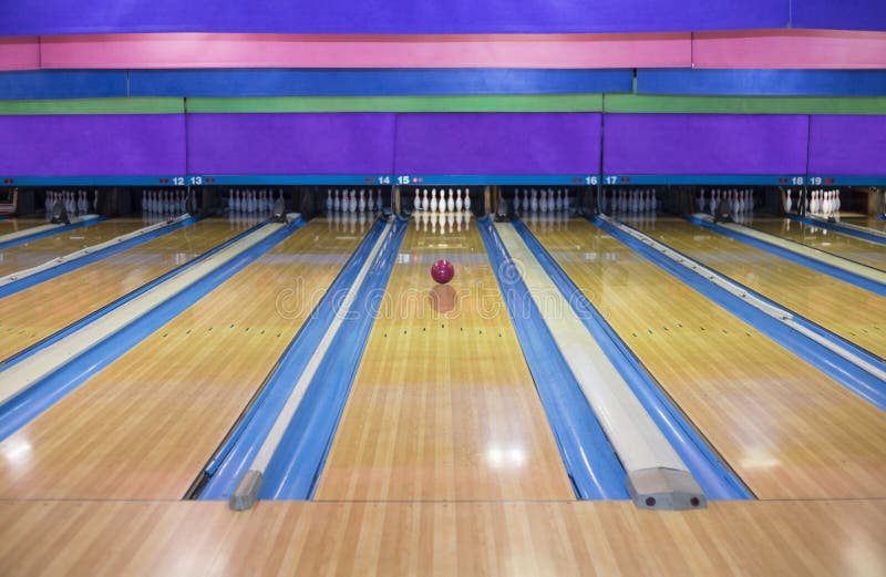 Large, brightly lit bowling alley with a red bowling ball rolling down the lane towards the white pins. Large, brightly lit bowling alley with a red bowling ball rolling down the lane towards the white pins