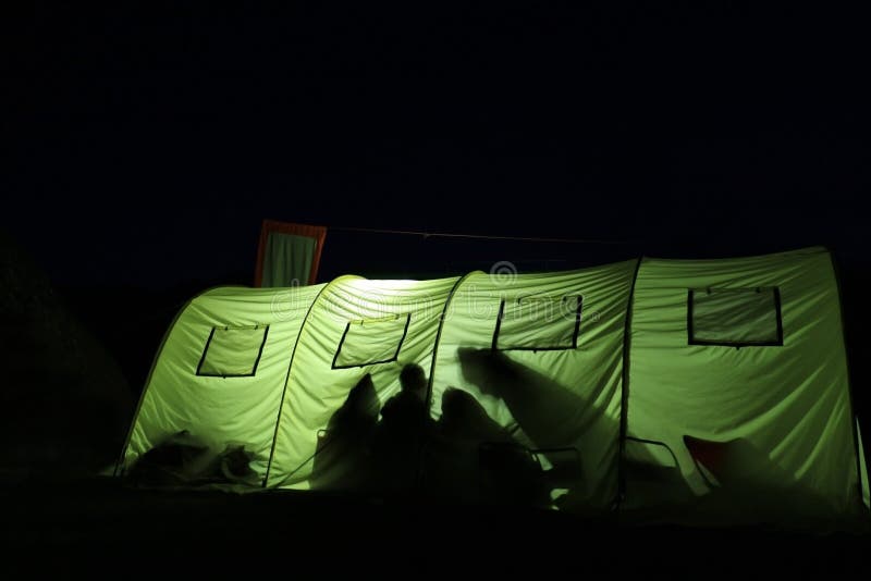 Big green tent at night lightened up from inside with shadows of people on the wall. Big green tent at night lightened up from inside with shadows of people on the wall