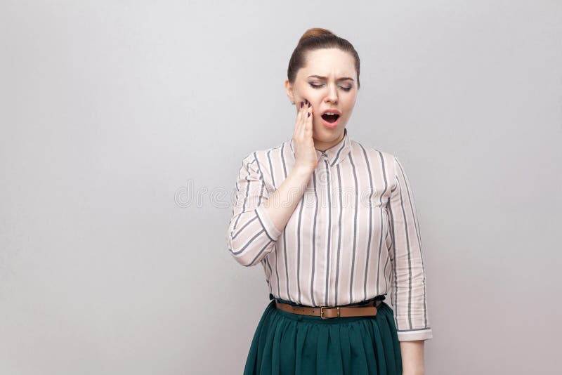 Боль зуба Портрет красивой молодой женщины в striped рубашке и зеленой юбке с собранным стилем причесок запрета, стоя и держа стоковое изображение rf Боль зуба Портрет красивой молодой женщины в striped рубашке и зеленой юбке с собранным стилем причесок запрета, стоя и держа стоковое изображение rf