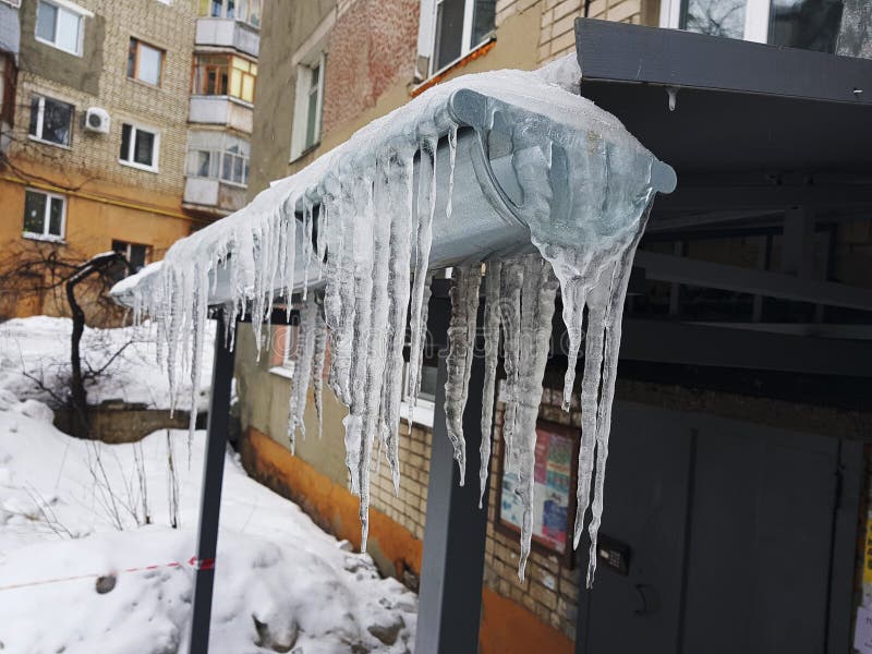 Большие опасные сосульки над входом к дому в зиме или весной против снега стоковое изображение