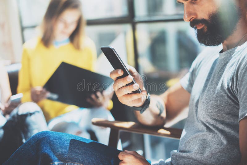 Бородатый человек битника используя современную руку Smartphone Собранные бизнесмены Yound совместно обсуждающ творческий город и стоковое фото Бородатый человек битника используя современную руку Smartphone Собранные бизнесмены Yound совместно обсуждающ творческий город и стоковое фото