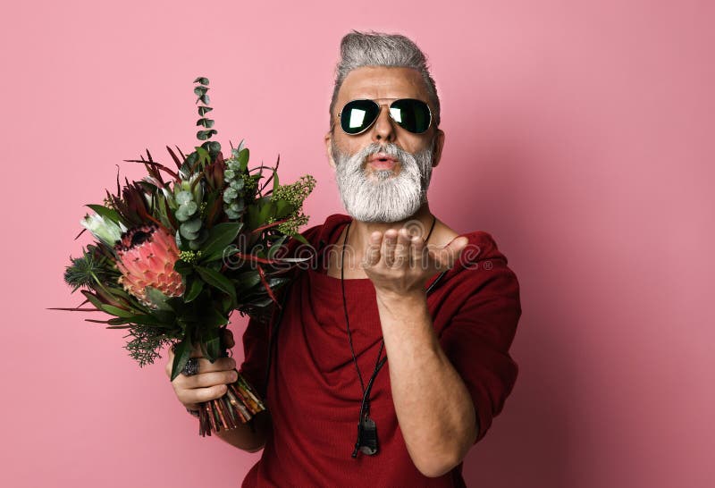 Stylish bearded middle-aged man with a modern hairstyle and fashionably dressed holding a bouquet of flowers and sending a kiss. Concept Valentine`s Day, Date. Stylish bearded middle-aged man with a modern hairstyle and fashionably dressed holding a bouquet of flowers and sending a kiss. Concept Valentine`s Day, Date