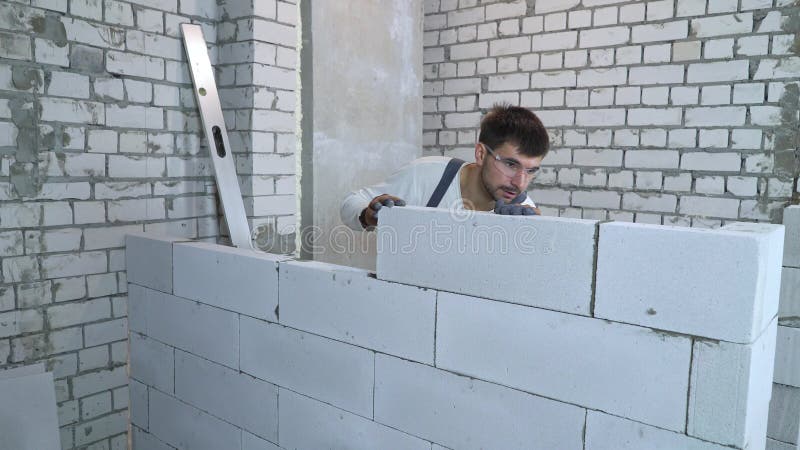 Бородатый строитель в рабочем одеянии и защитные очки, закладывающие блоки видеоматериал