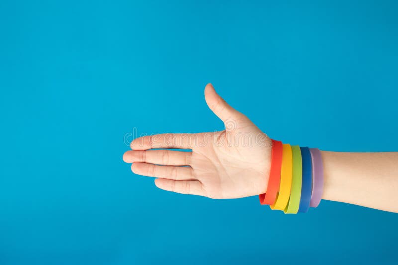 Браслет wristband флага LGBT радуги на женской руке на голубой предпосылке стоковая фотография Браслет wristband флага LGBT радуги на женской руке на голубой предпосылке стоковая фотография