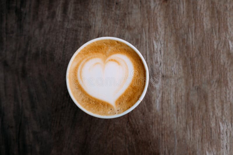 Бумажный стаканчик капучино с красивым искусством latte в форме сердца на деревянной предпосылке E стоковая фотография Бумажный стаканчик капучино с красивым искусством latte в форме сердца на деревянной предпосылке E стоковая фотография
