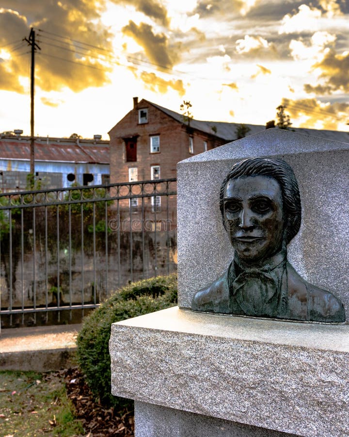 Prattville, Alabama, USA - December 26, 2016: Bust of Daniel Pratt the founder of Prattville with the Continental Eagle Cotton Gin Company in the background. Prattville, Alabama, USA - December 26, 2016: Bust of Daniel Pratt the founder of Prattville with the Continental Eagle Cotton Gin Company in the background.