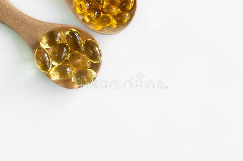 At the top of the edge there are 2 wooden spoons with capsules of fish fat Omega-3 and vitamin D3 large and small. Top view and free space for text. Isolated. At the top of the edge there are 2 wooden spoons with capsules of fish fat Omega-3 and vitamin D3 large and small. Top view and free space for text. Isolated