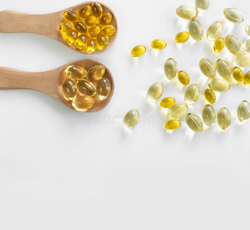 At the top left, 2 wooden spoons with capsules of fish fat Omega-3 and vitamin D3 and several capsules are scattered. Top view and free space for text. Isolated on white background. At the top left, 2 wooden spoons with capsules of fish fat Omega-3 and vitamin D3 and several capsules are scattered. Top view and free space for text. Isolated on white background