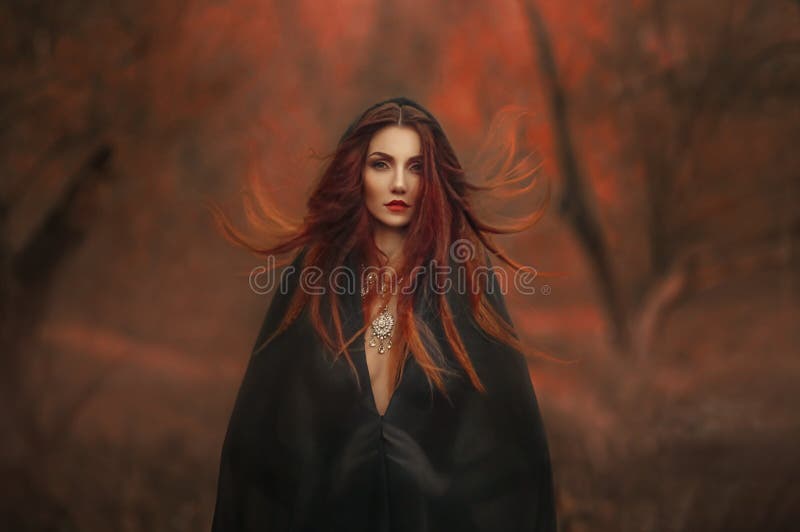 Ведьма готической женщины фантазии темная. Redhaired злой демон девушки в черном капюшоне мыса платья. Длинные волосы порхают лета стоковая фотография rf