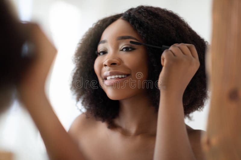 Gorgeous black woman applying mascara on her lashes in front of mirror at home. Attractive African American lady using decorative cosmetics, making her daily routine, pampering herself. Gorgeous black woman applying mascara on her lashes in front of mirror at home. Attractive African American lady using decorative cosmetics, making her daily routine, pampering herself