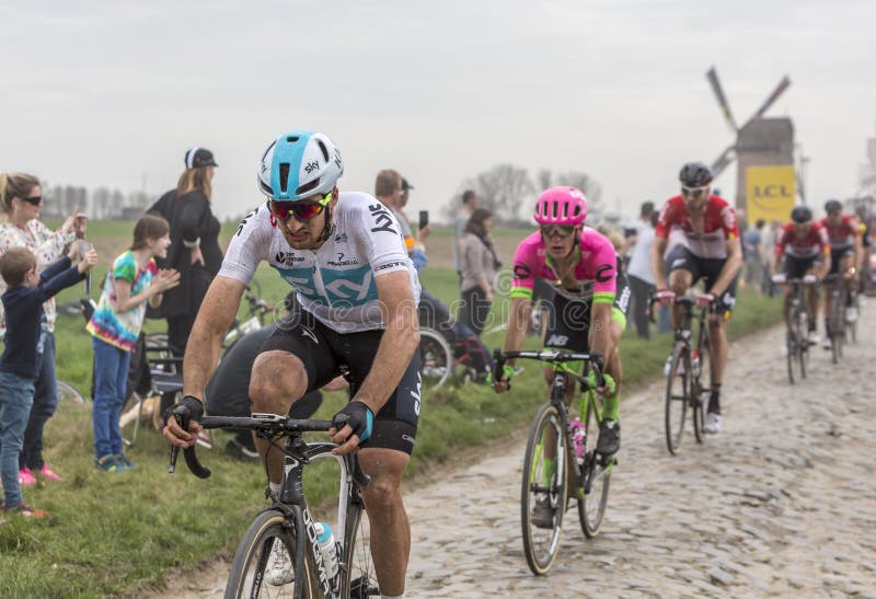 Templeuve, France - April 08, 2018: The Italian cyclist Gianni Moscon of Team Sky riding in the peloton on the cobblestone road in Templeuve in front of the traditional Vertain Windmill during Paris-Roubaix 2018. Templeuve, France - April 08, 2018: The Italian cyclist Gianni Moscon of Team Sky riding in the peloton on the cobblestone road in Templeuve in front of the traditional Vertain Windmill during Paris-Roubaix 2018.