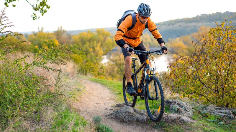Cyclist in Orange Riding the Mountain Bike on the Autumn Rocky Enduro Trail. Extreme Sport and Enduro Biking Concept. Cyclist in Orange Riding the Mountain Bike on the Autumn Rocky Enduro Trail. Extreme Sport and Enduro Biking Concept.