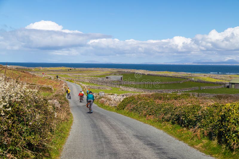 INISHMORE, REPUBLIC OF IRELAND - 6H APRIL 23: Cyclists on a road on Inishmore island, part of the Aran Islands. Cycling is a popular way to explore this destination. INISHMORE, REPUBLIC OF IRELAND - 6H APRIL 23: Cyclists on a road on Inishmore island, part of the Aran Islands. Cycling is a popular way to explore this destination